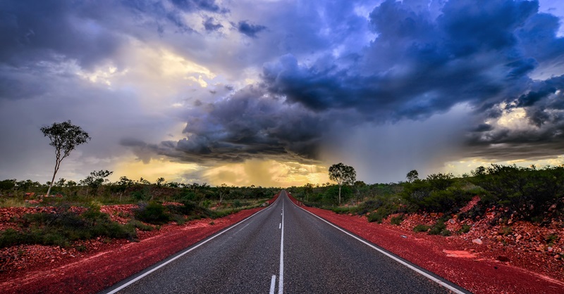 storm clouds over an outback highway fringed with red dirt