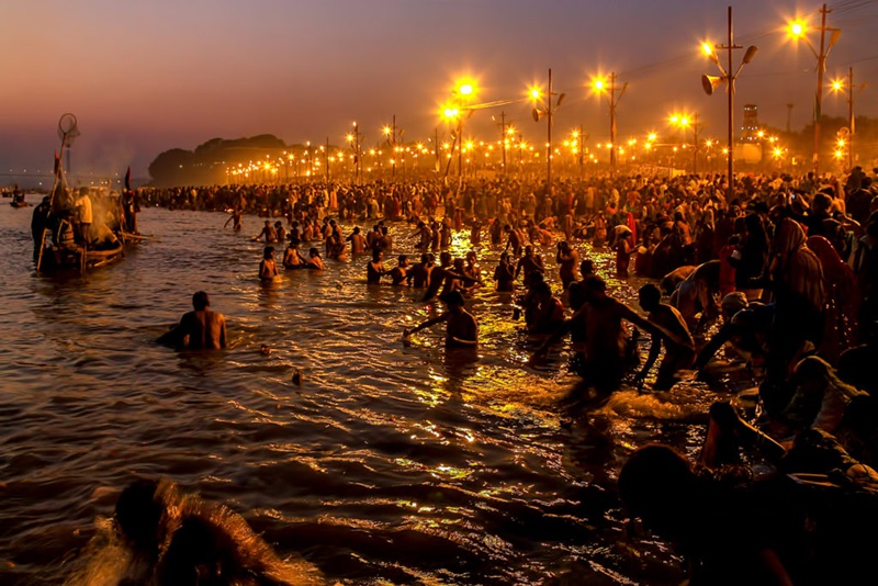 People entering a river at night with lights along banks