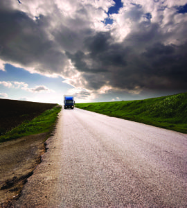 Truck driving along a road with clouds above