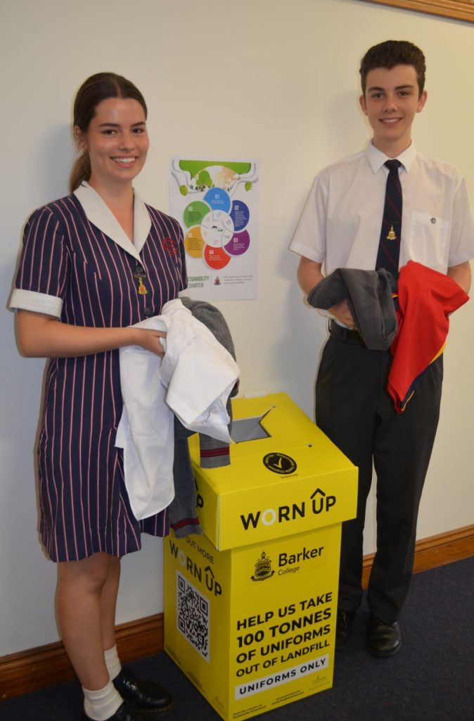two students hold uniforms next to a Worn Up box. The fabrics from the uniforms are being turned into furniture, building a circular economy