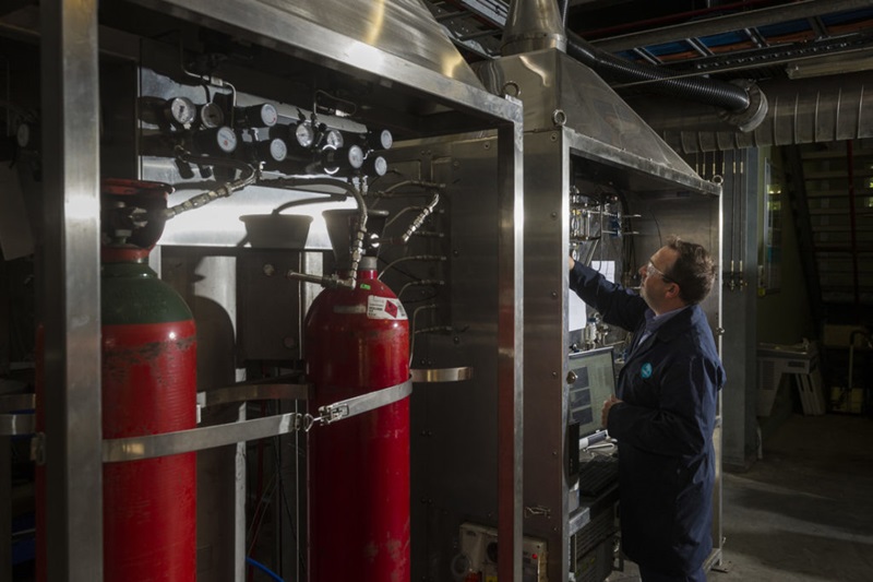 A man standing next to large red cylinders, reaching for something in a lab.