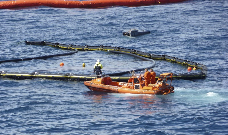 A person in a boat checks up on oil spill response skimming rings on the ocean's surface