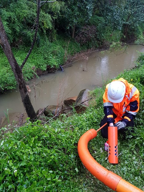 man in hard hat beside river inserting device into pipe