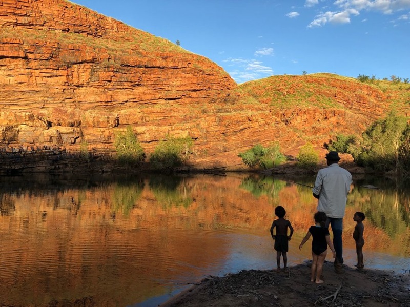 Three kids and one man stand by a waterhole