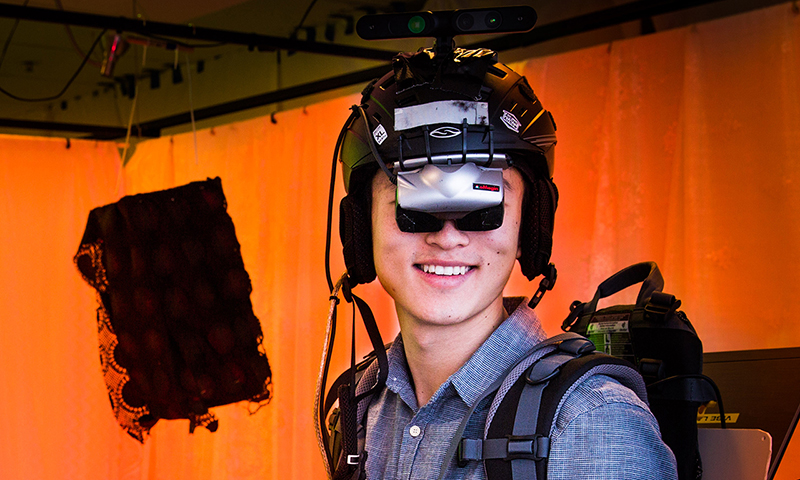 A young man wearing a VR headset stands in a room with a back light orange curtain.