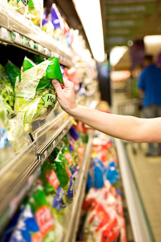 An arm reaches out for a packaged salad in a supermarket aisle.