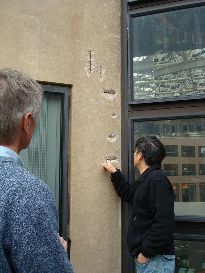 Two men inspecting a concrete wall with signs of deterioration