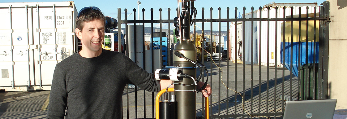 Nick Hardman-Mountford standing on a warf, resting arm on a BioArgo robotic float.