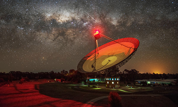Parkes radio telescope at night lit up by lights. 