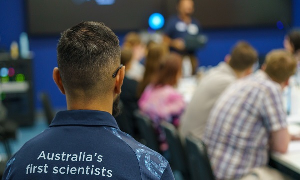 Meeting room with Indigenous graduates listening to a speaker. Person in foreground wears a CSIRO tshirt that says 'Australia's first scientists'.