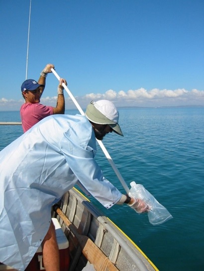 Two people leaning over the side of a boat taking water samples.