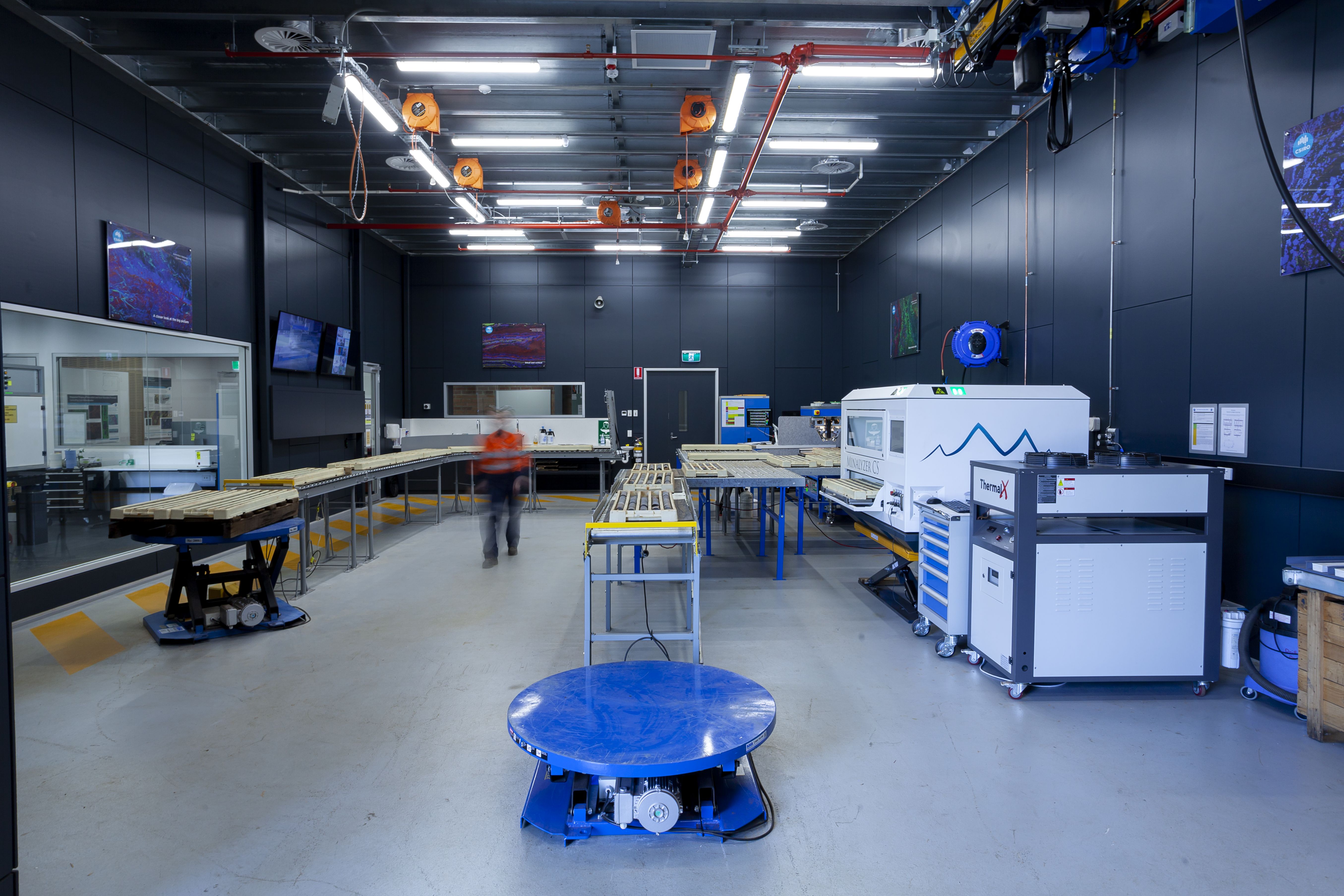 An open warehouse-style laboratory with long bench conveyors and instruments along wall
