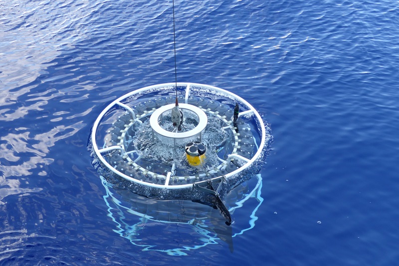 A CTD instrument, or rosette of Niskin bottles, is breaking the surface of the ocean as it is pulled up from depth.