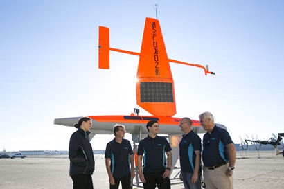 Five CSIRO staff stand in-front of an orange Saildrone